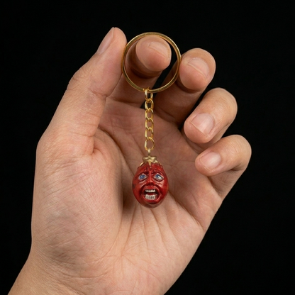 Hand holding a keychain with a red skull pendant against a black background